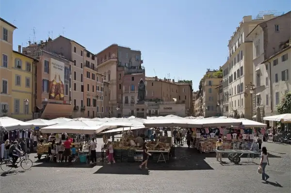 Der Campo de' Fiori Platz in Rom, Italien, bei Tag, mit Statuen und Gebäuden im Hintergrund.