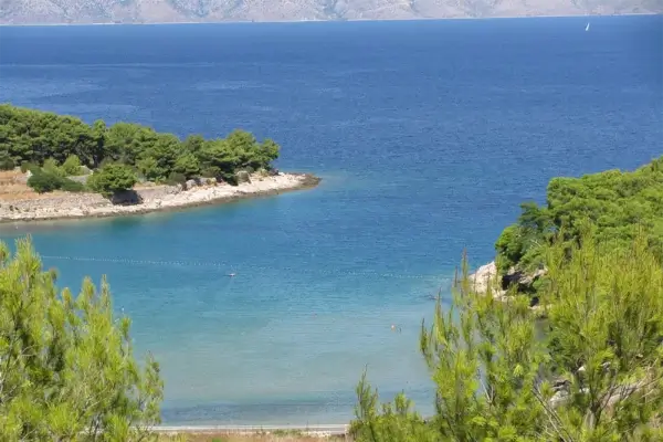 Blick auf den Grebišće-Strand und das Meer umgeben mediterraner Vegetation.