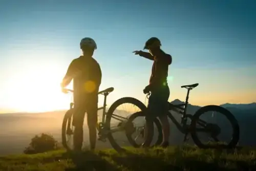 Zwei Menschen stehen neben Mountainbikes, reden und beobachten die Aussicht im Hintergrund.