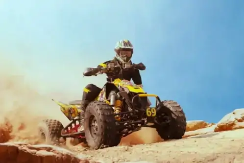 Ein Mann sitzt mit Helm und Brille auf einem Quad in den Bergen.