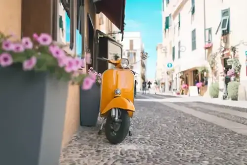 Orangefarbener Oldtimer-Roller steht in der Straße von Alghero. Sardinien. Italien.
