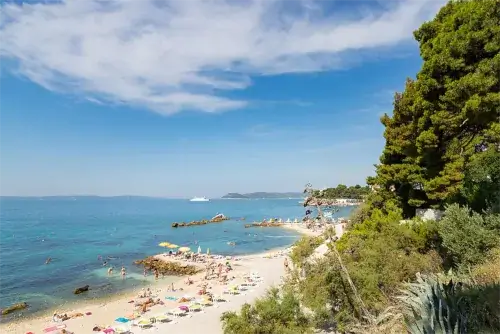 Luftaufnahme vom Strand Ovčice in Split mit klarem Wasser, Badegästen und umliegender Küstenlandschaft.